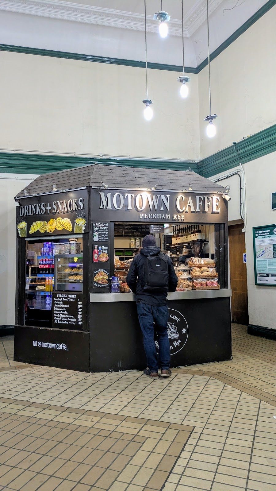 The Motown Caffe kiosk inside the tiled station concourse at Station Way, with a customer waiting at the counter.